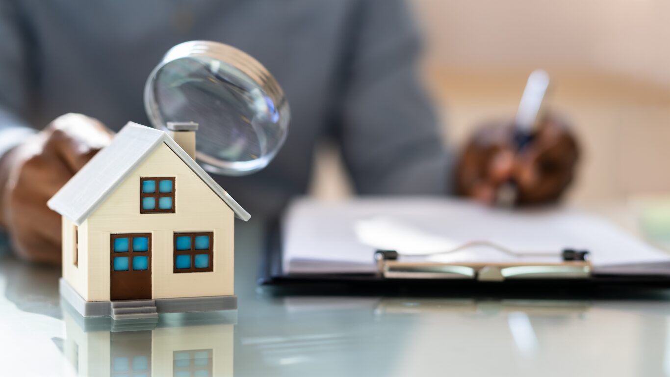 Model house on a desk beside a magnifying glass and paperwork
